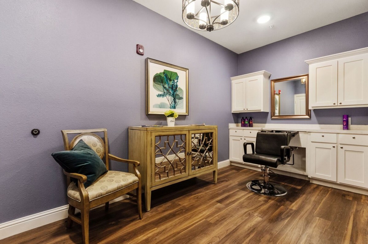 A stylish salon room with modern decor, featuring a comfortable chair, artwork on the wall, and elegant wood flooring.