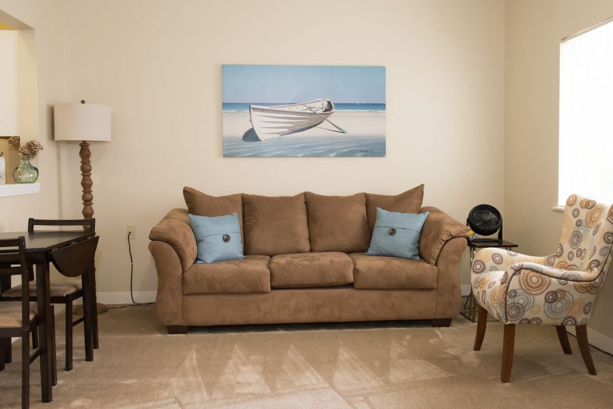A cozy living room with a brown sofa, adorned with blue cushions and a boat painting on the wall.