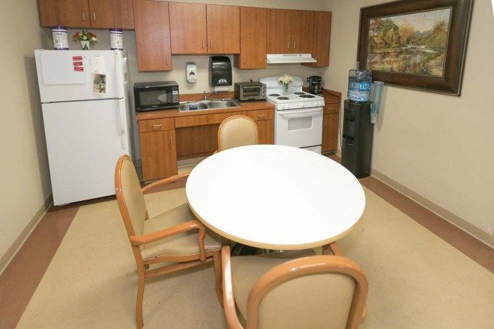 A cozy kitchen area with a round table and chairs, equipped with various appliances and a water cooler.