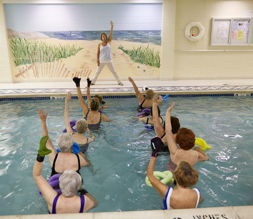 A lively water aerobics class in an indoor pool, led by an instructor as participants engage in exercise.