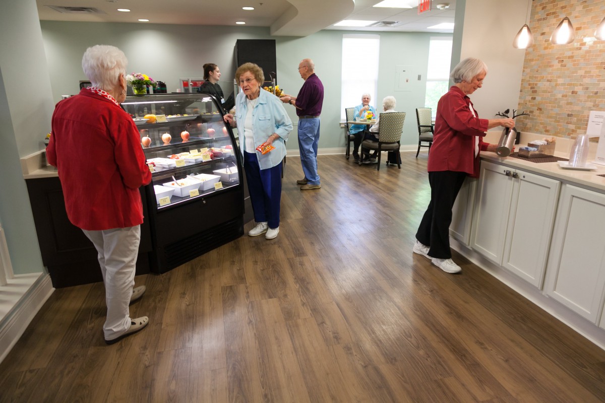 Senior citizens socializing in a cafe with a food display counter.