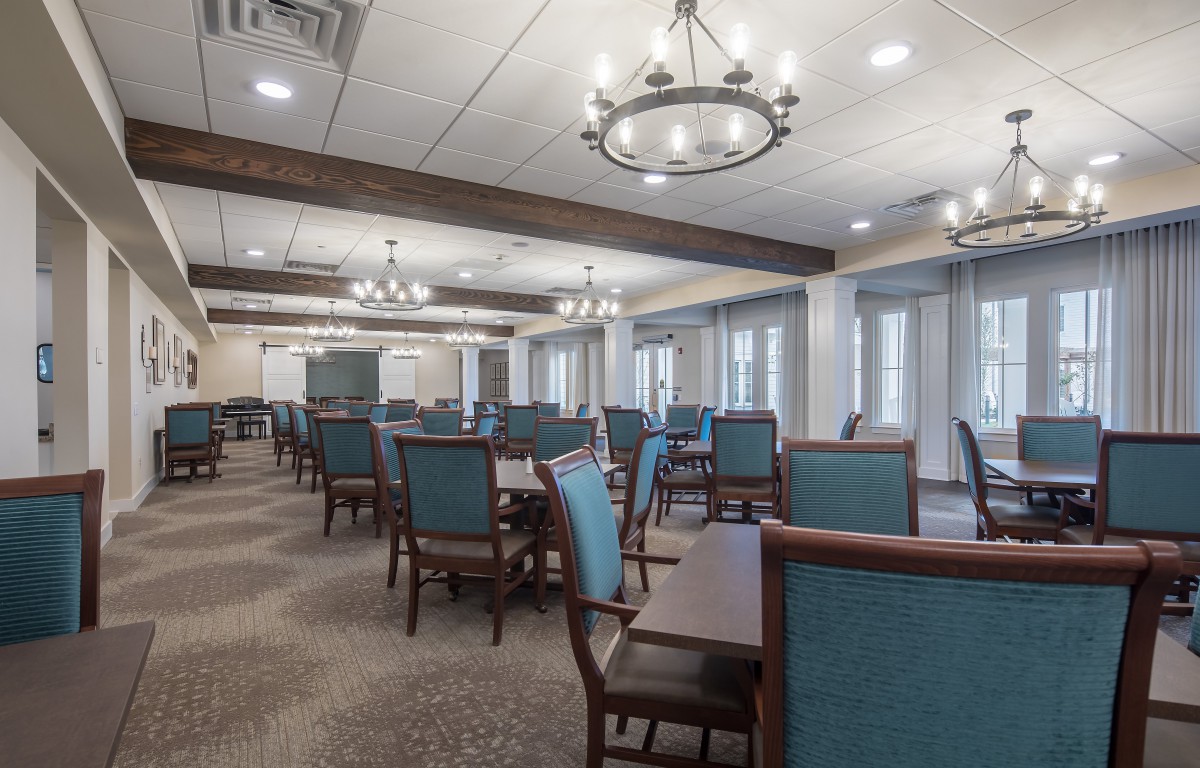 A spacious dining area with elegant chandeliers and neatly arranged tables and chairs.