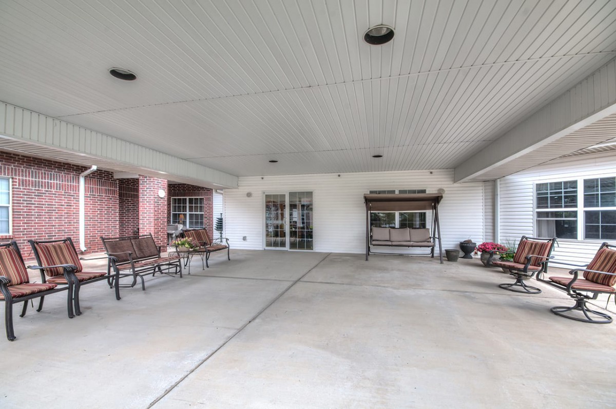 A covered entrance area with benches and a swing, featuring a concrete floor outside a building.