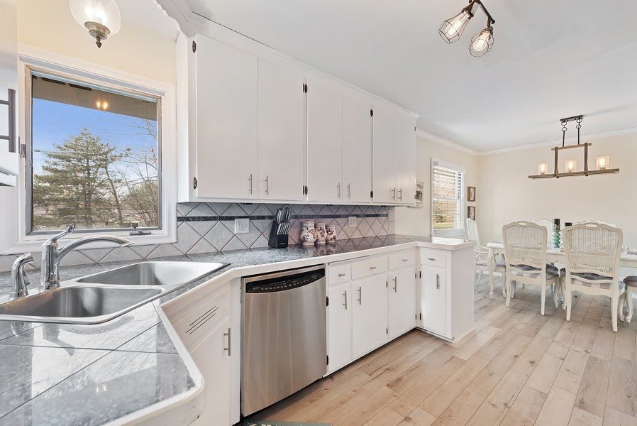 A modern kitchen with white cabinets, stainless steel appliances, and hardwood flooring.