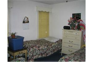 A bedroom featuring twin beds with floral bedding, a dresser with decorative items, and a window with yellow curtains.