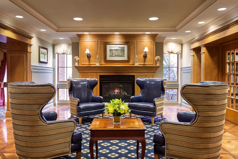 A cozy lounge area featuring blue armchairs, a central fireplace, and a wooden coffee table with fresh flowers.