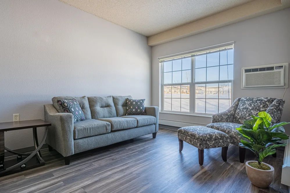 A cozy living room with a sofa, chair, and ottoman by a large window.
