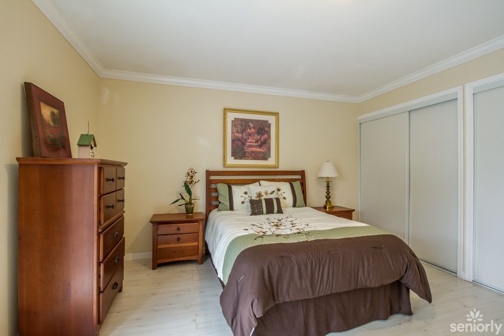 A cozy bedroom featuring a neatly made bed, with wooden furniture including a dresser and nightstand, adorned with decorative elements.