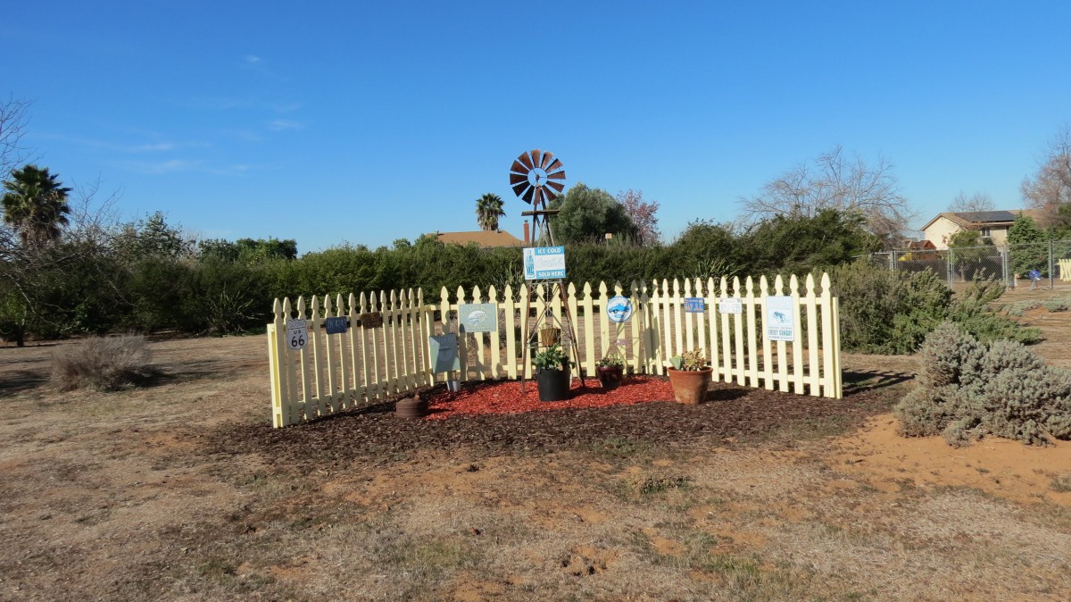A small fenced garden with a variety of plants, featuring a decorative windmill in the background.