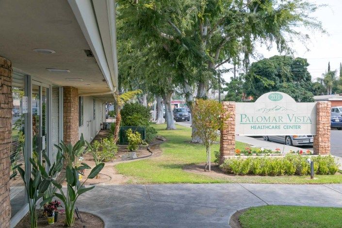 A peaceful outdoor setting with a pathway lined by greenery and a sign near a building.