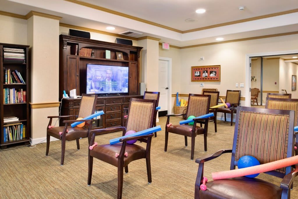 A communal room with chairs arranged in front of a television, each chair equipped with exercise equipment.