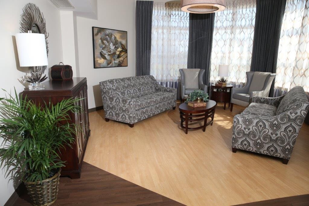 A cozy living room with patterned sofas, armchairs, and a coffee table, complemented by decorative plants and elegant curtains.