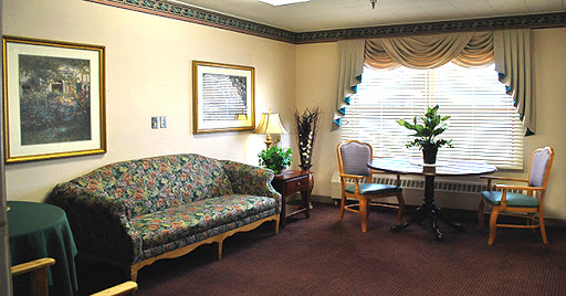 A cozy living room setup featuring a floral patterned sofa, a wooden table and chair, along with decorative plants and wall art.