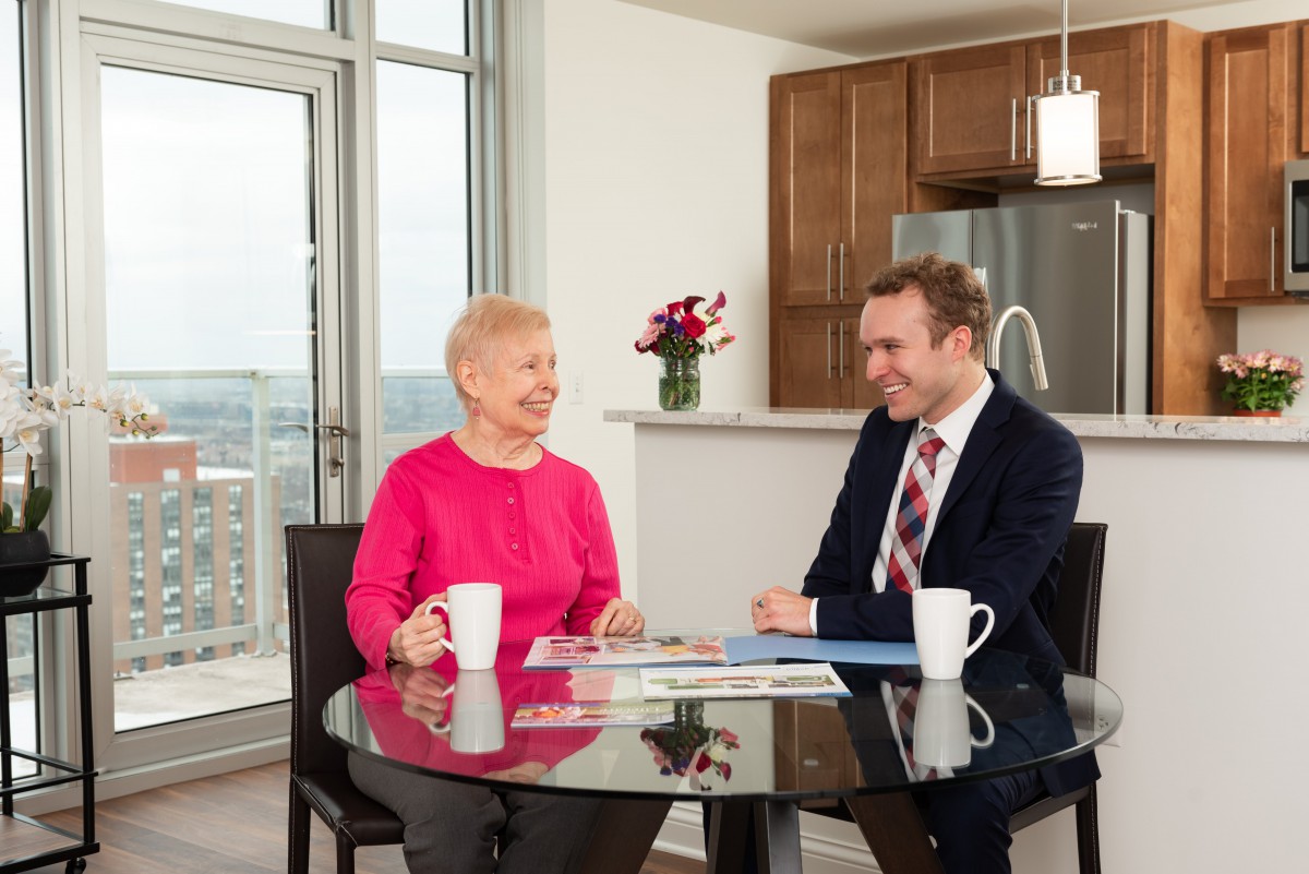 A senior woman and a man having a discussion at a table in a modern kitchen setting.
