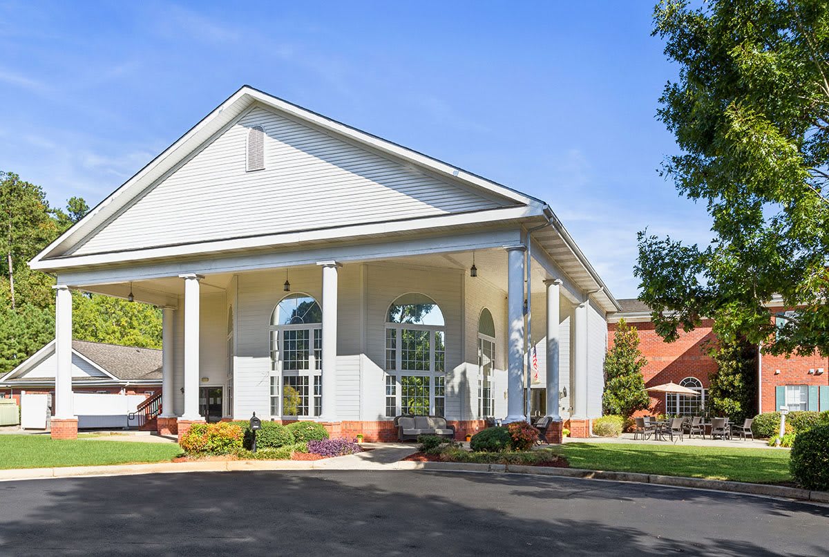A large white building with columns and a driveway surrounded by trees.