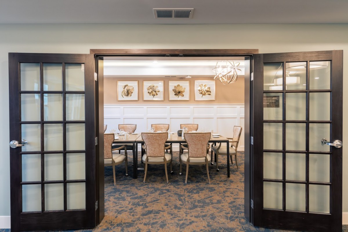 A well-lit dining room with a large table surrounded by chairs, decorated with framed artwork on the walls.