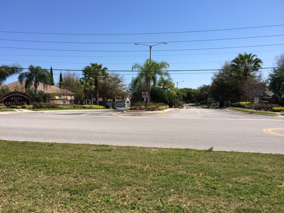 A quiet residential street intersection with palm trees and houses under a clear blue sky.