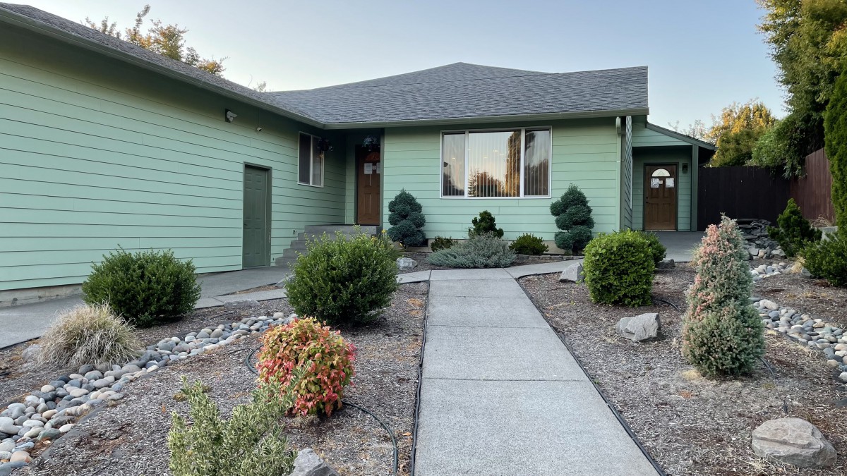 A residential house with a green exterior and well-maintained landscaping along a concrete pathway.