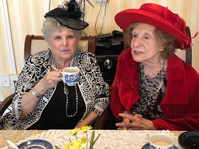 Two elderly women enjoying a tea party, wearing stylish hats.