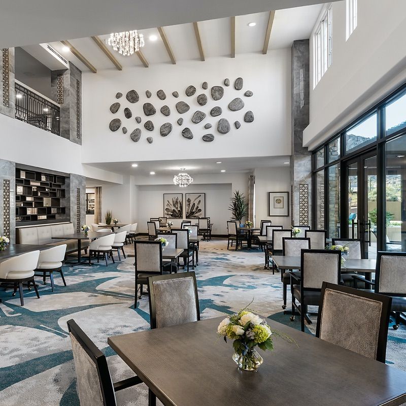 A modern dining area with high ceilings, decorative wall art, and ample natural light from large windows.