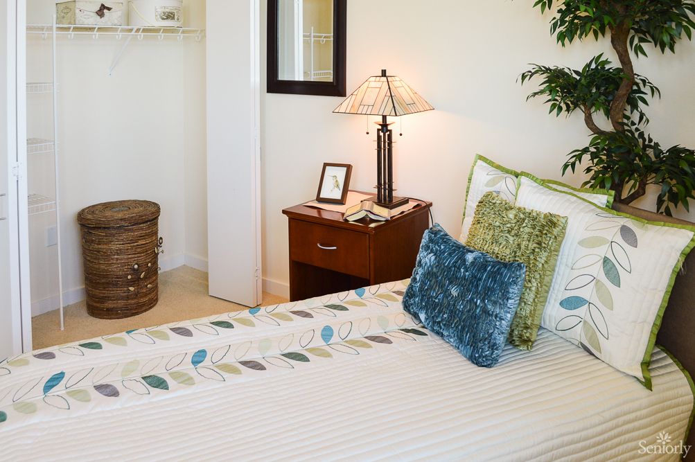 A cozy bedroom interior featuring a neatly made bed with decorative pillows and a nightstand adorned with a lamp.