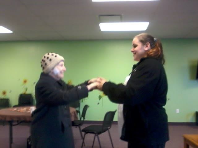 Two people standing indoors, holding hands in a friendly interaction.