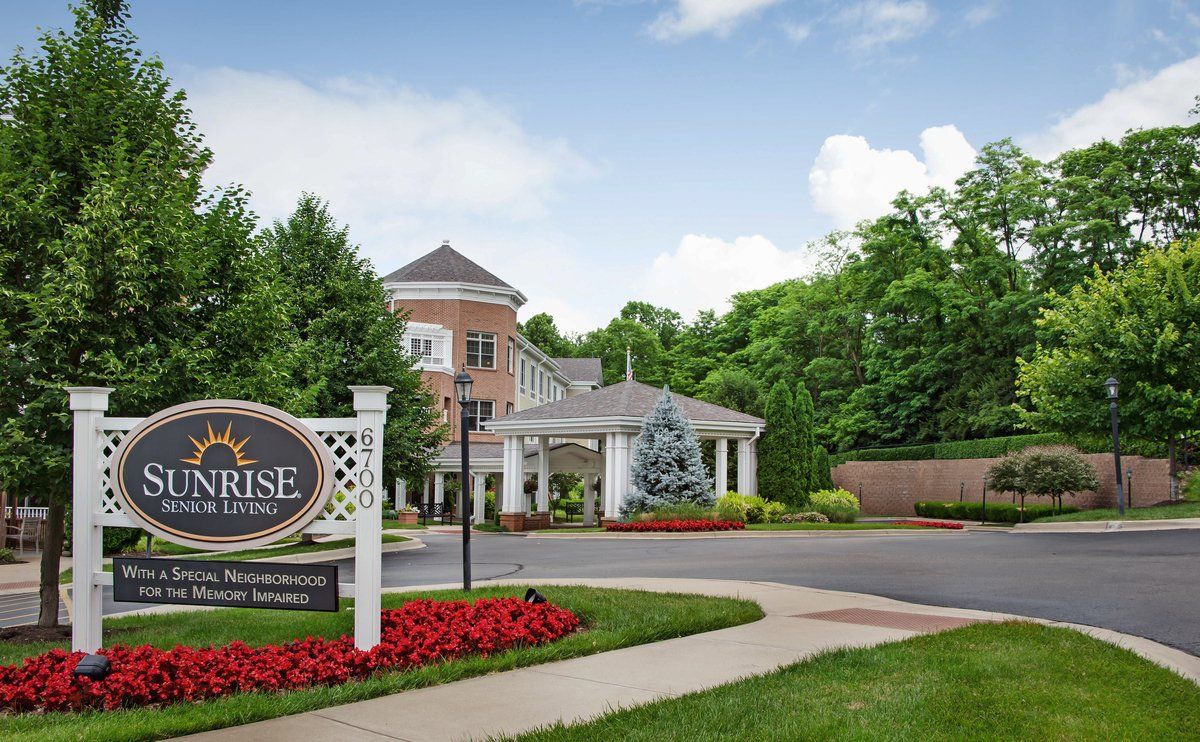 Entrance to a landscaped building with a sign and surrounding greenery.