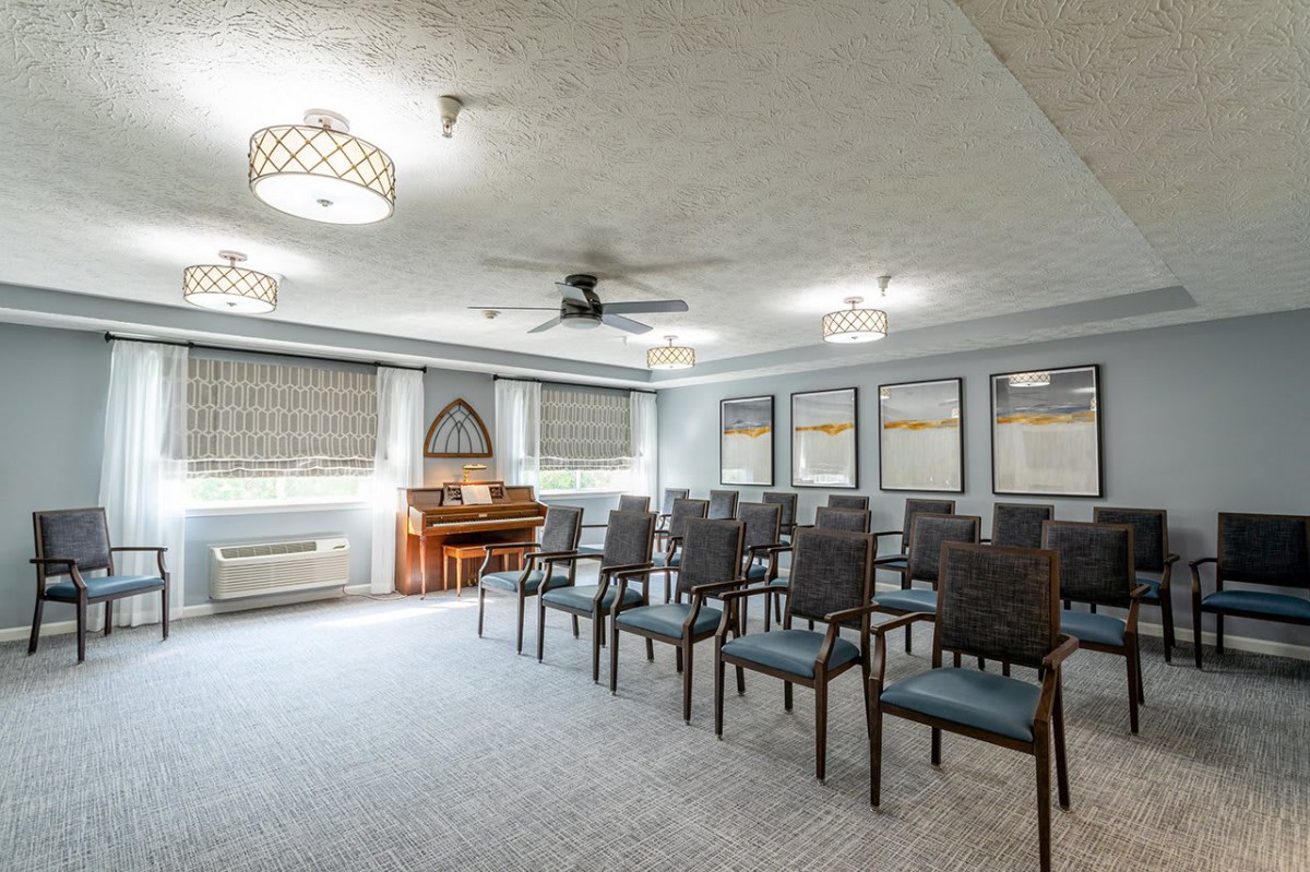 A well-lit meeting room with rows of chairs, a piano, and large windows.