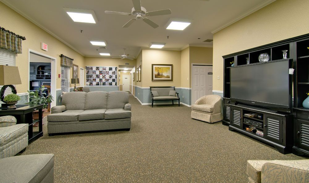 A comfortable lounge area featuring sofas, armchairs, a television, and a ceiling fan.