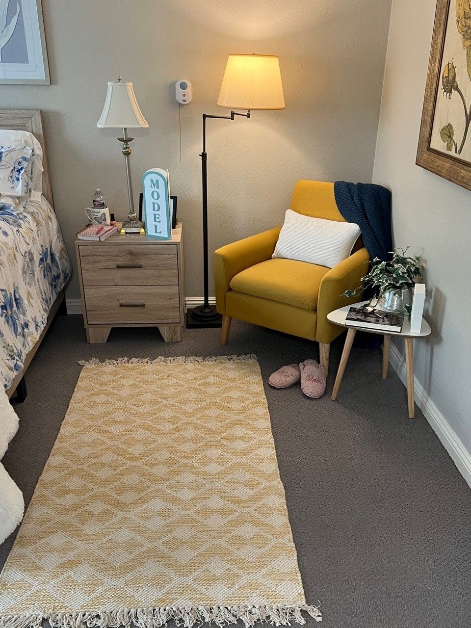 A cozy bedroom corner featuring a yellow chair, floor lamp, and nightstand beside a bed with decorative bedding.