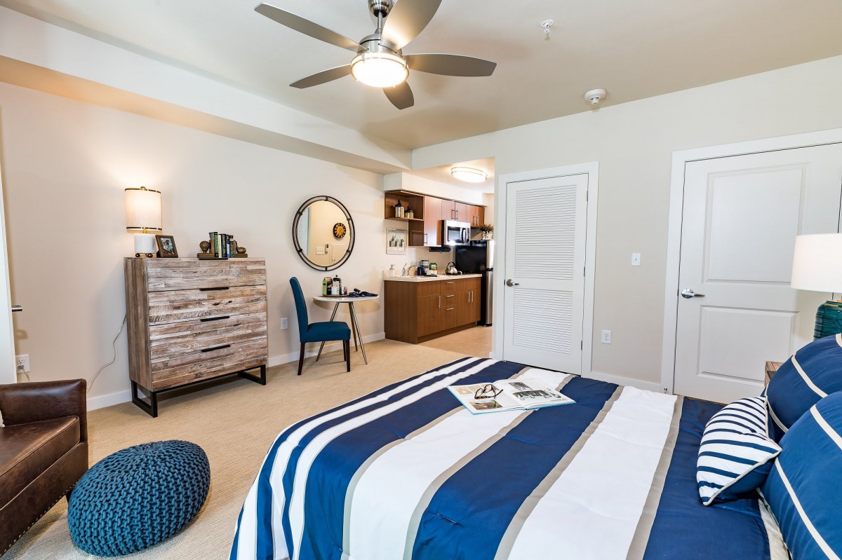 A modern bedroom with striped bedding, featuring a ceiling fan and stylish decor.