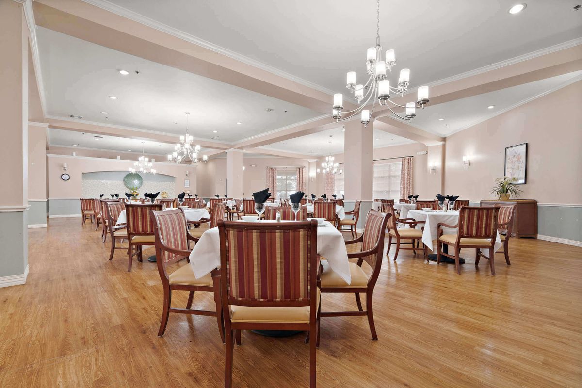 An elegant dining room with neatly arranged tables and chairs, illuminated by chandeliers.