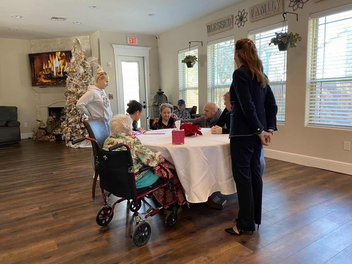 A group of people gathered around a table in a care home setting, engaging in conversation.