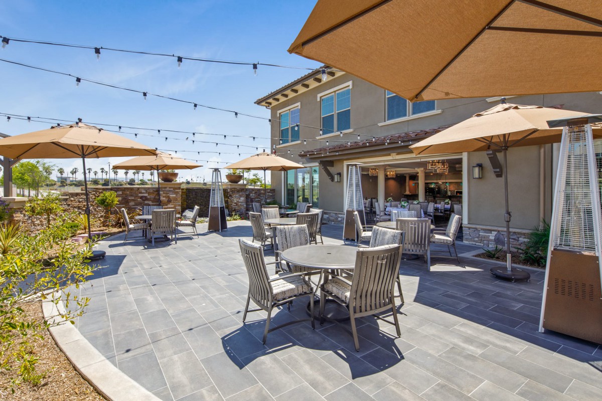 A spacious outdoor patio with modern furniture, string lights, and large umbrellas under a clear blue sky.
