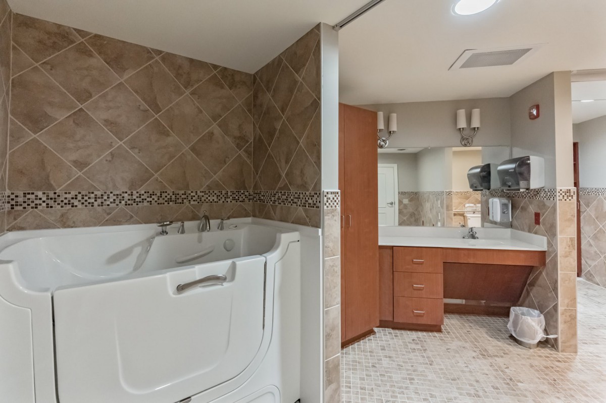 A modern bathroom featuring a walk-in bathtub, tiled walls, and a vanity with a large mirror and wooden cabinets.