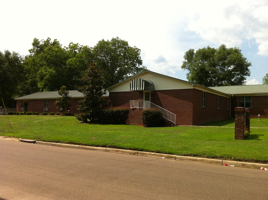 A brick building surrounded by trees and a well-maintained lawn.