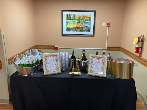 A beautifully arranged beverage station for a celebration, featuring wine bottles, glasses, and framed menus.