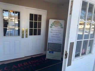 An open entrance door leading to a building, with a sign displayed beside it.