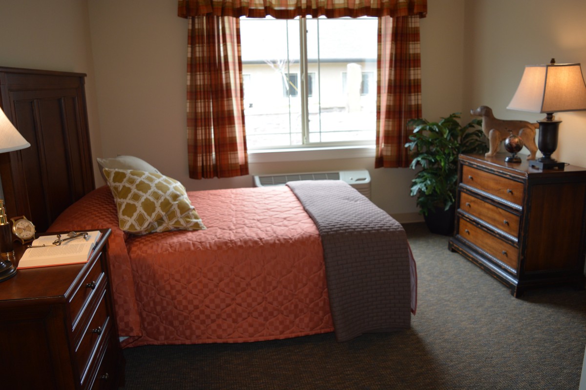 A cozy bedroom with a neatly made bed, colorful curtains, and a window letting in natural light.
