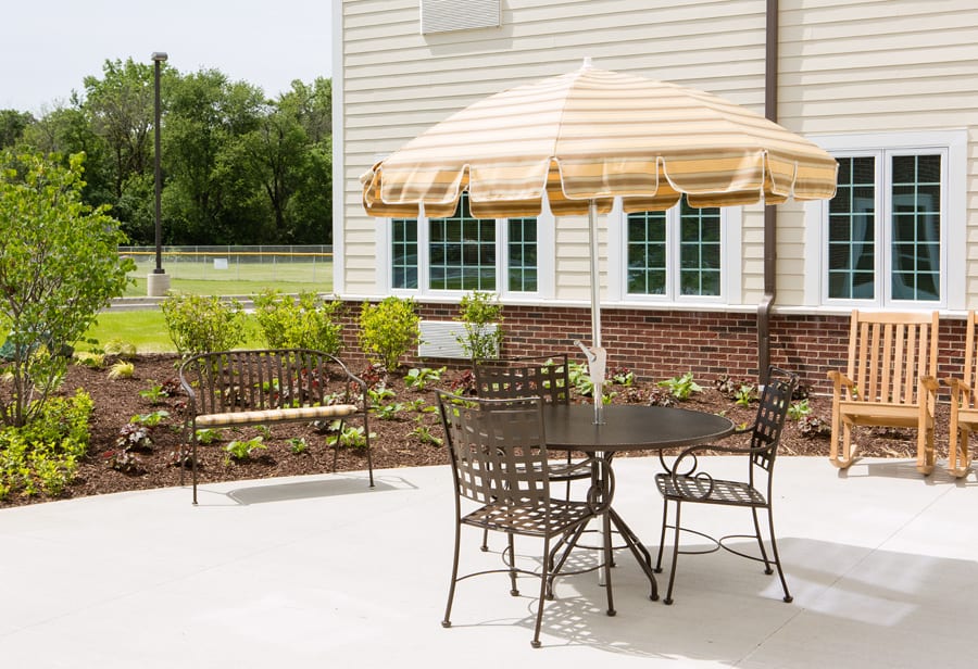 A backyard patio with metal furniture and a striped umbrella.