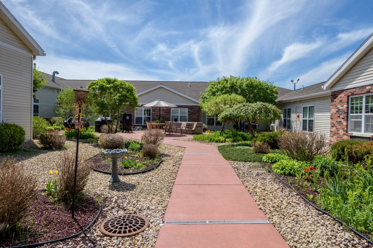 A beautifully landscaped garden with a red pathway leading to a single-story building under a blue sky.