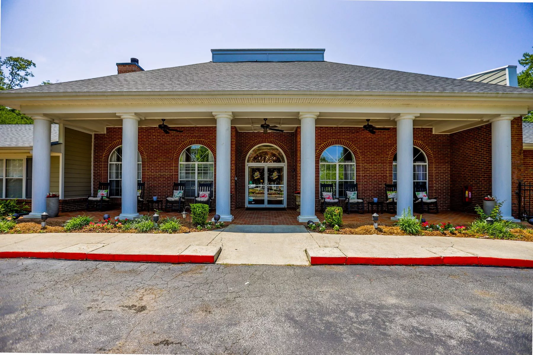 A brick building with large white columns at the entrance and a neatly landscaped area in front.