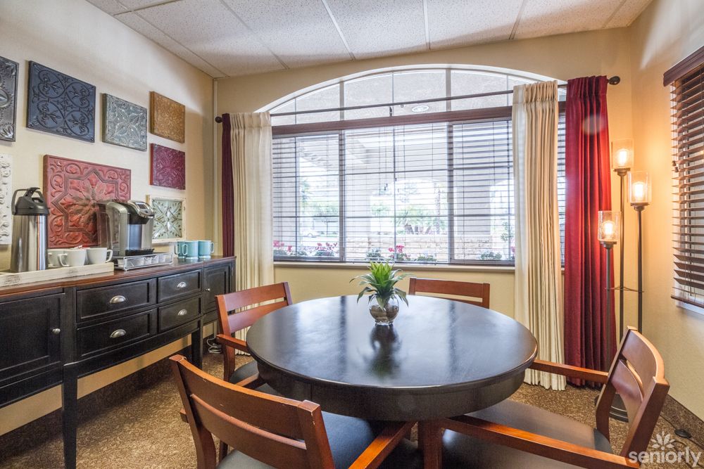 A well-lit meeting room with a round table and chairs by a large window with blinds.