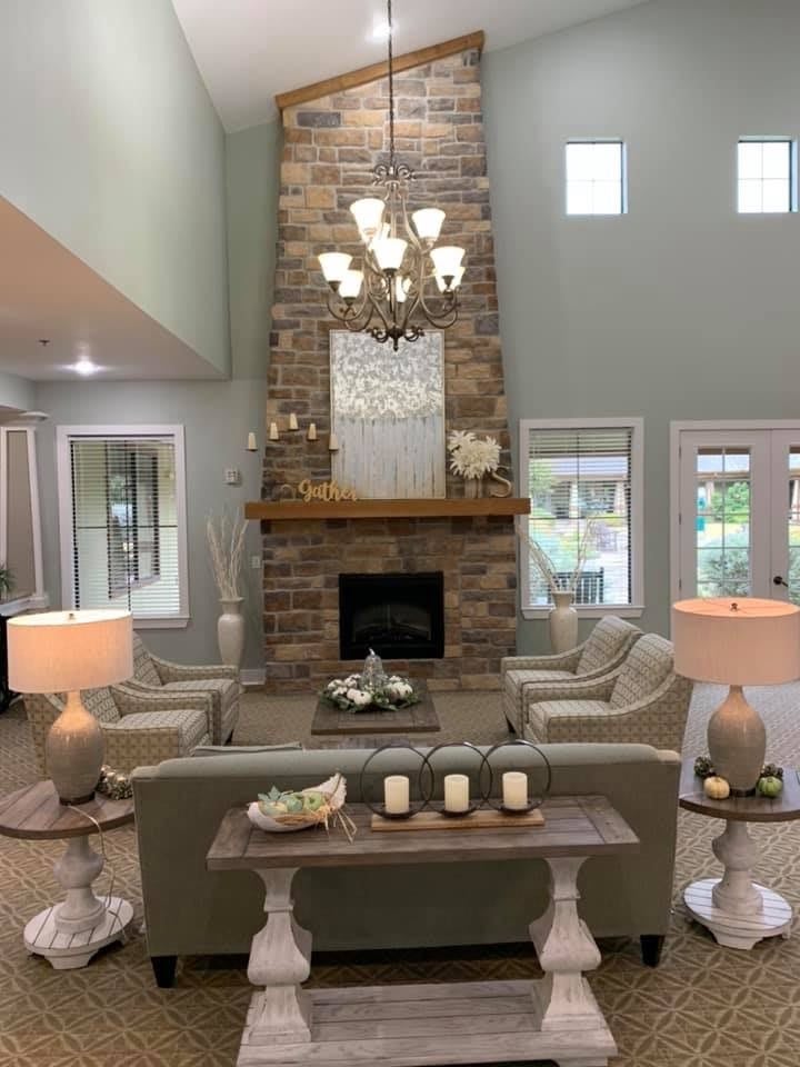 A modern living room featuring a tall stone fireplace and elegant chandelier, surrounded by comfortable seating.