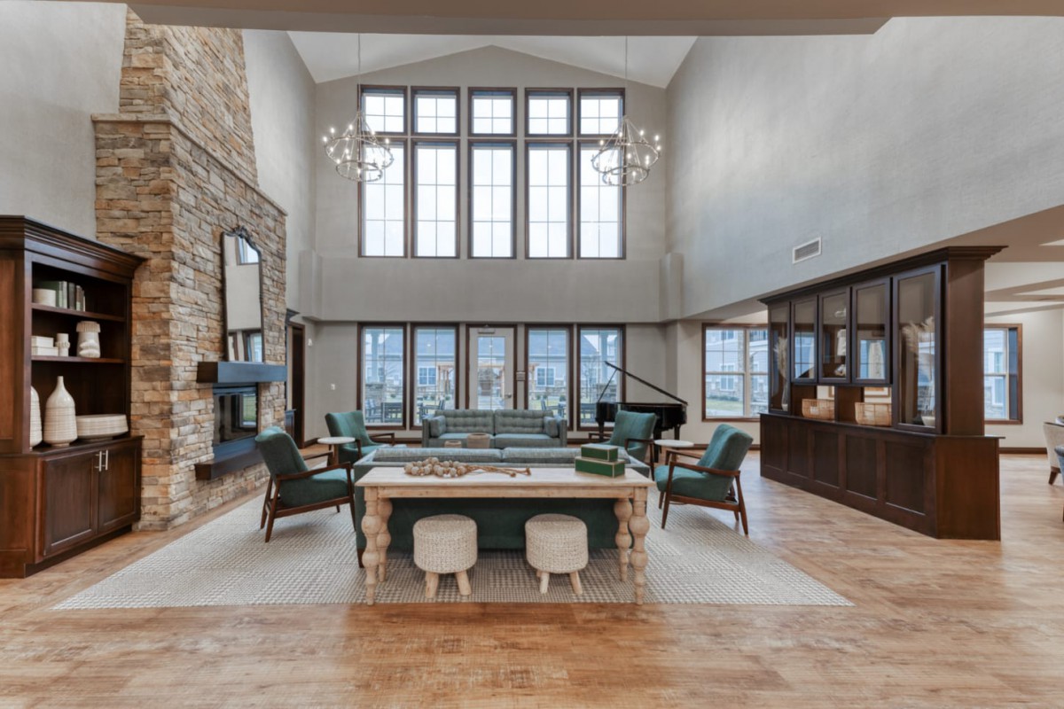 A spacious and luxurious living room with high ceilings, large windows, a stone fireplace, and elegant chandeliers.