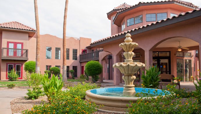 A beautiful courtyard with a central fountain surrounded by greenery and a large building.