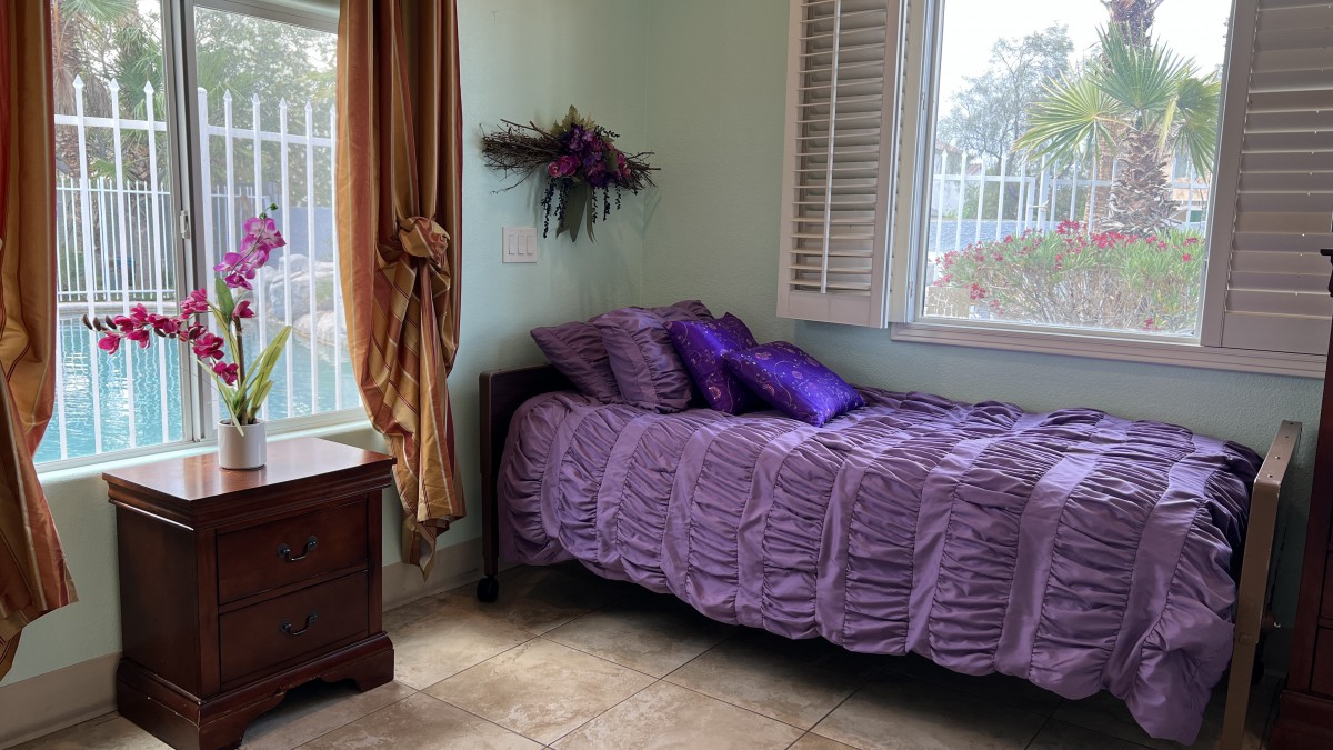Cozy bedroom with a purple-themed single bed and natural lighting.