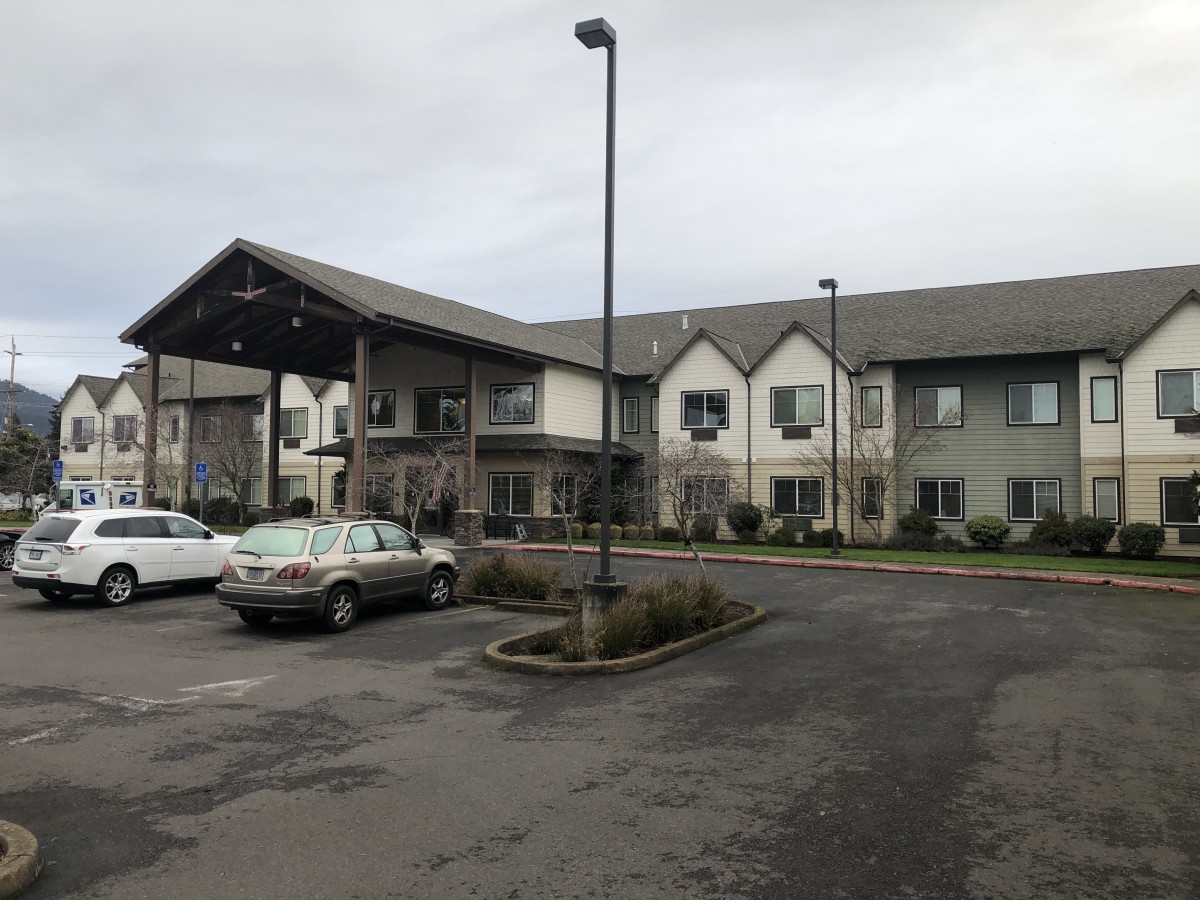 A two-story building with a parking lot and several cars on an overcast day.