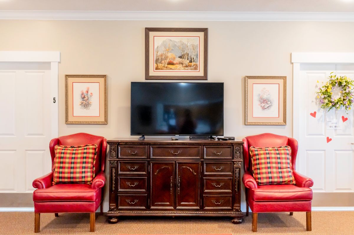 A stylish living room setup featuring a television on a wooden cabinet, flanked by red armchairs and framed artwork.