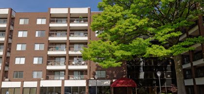 A multi-story apartment building with balconies and a large green tree in front.